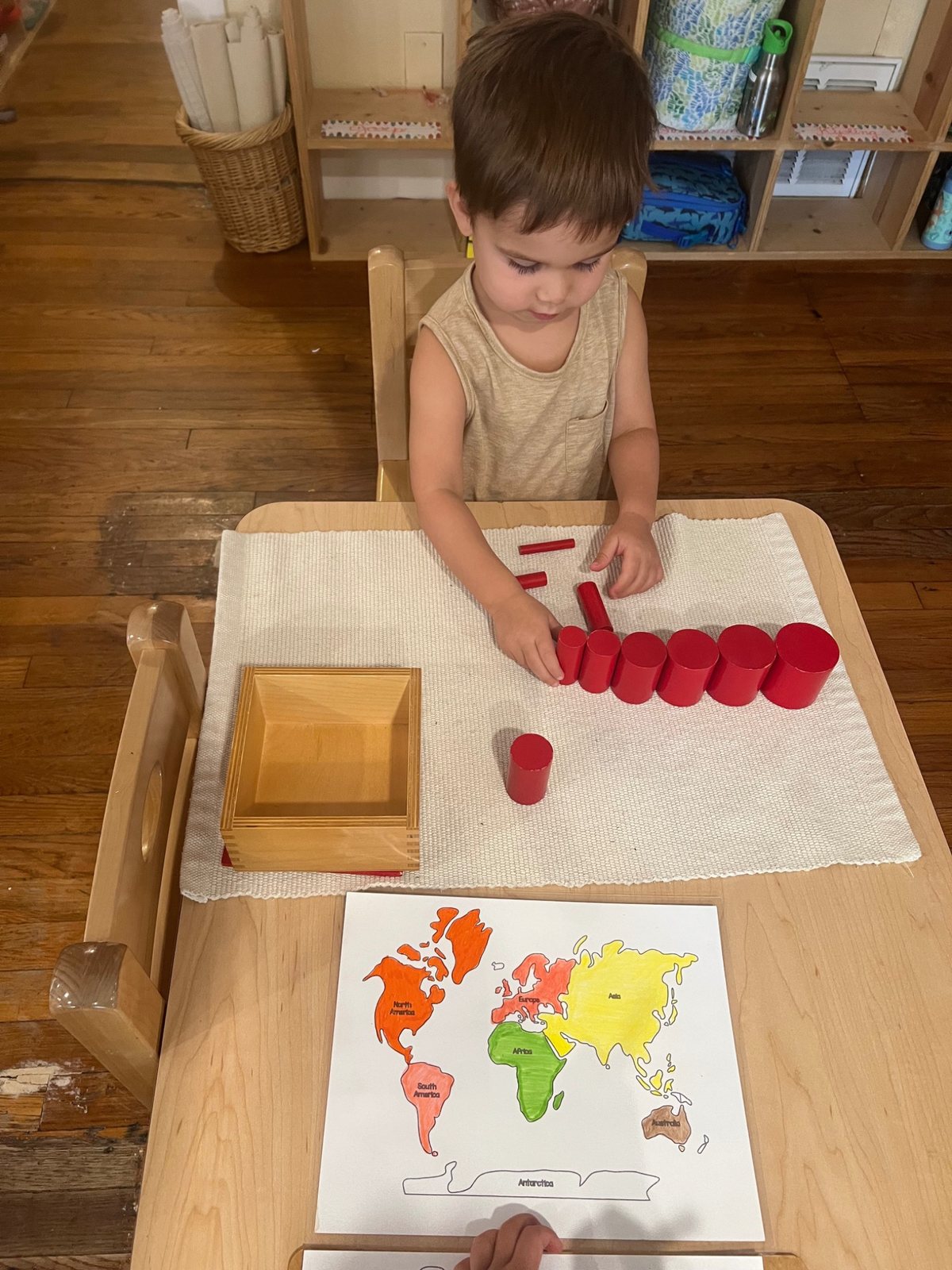 A child arranging red cylinders beside a world map.