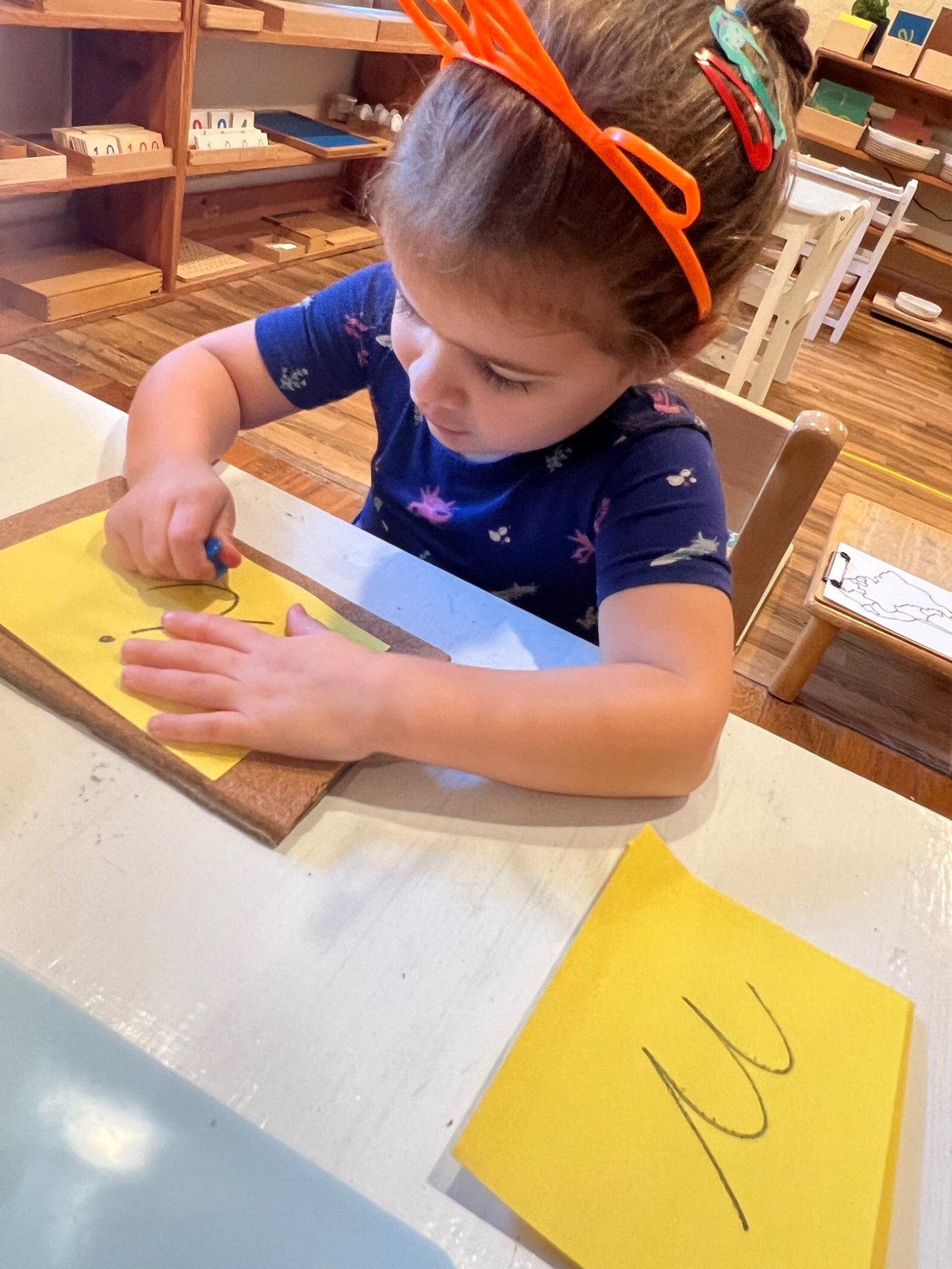 A child practicing writing on yellow paper at a classroom table.