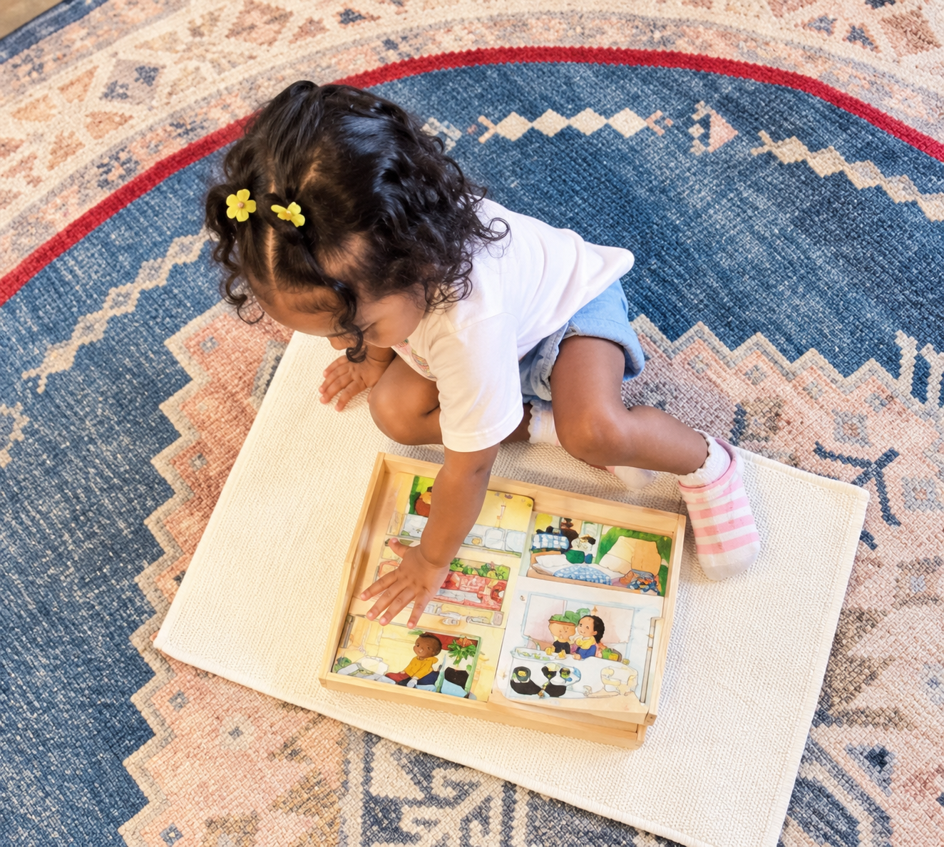 A toddler exploring an illustrated picture book on a classroom rug.