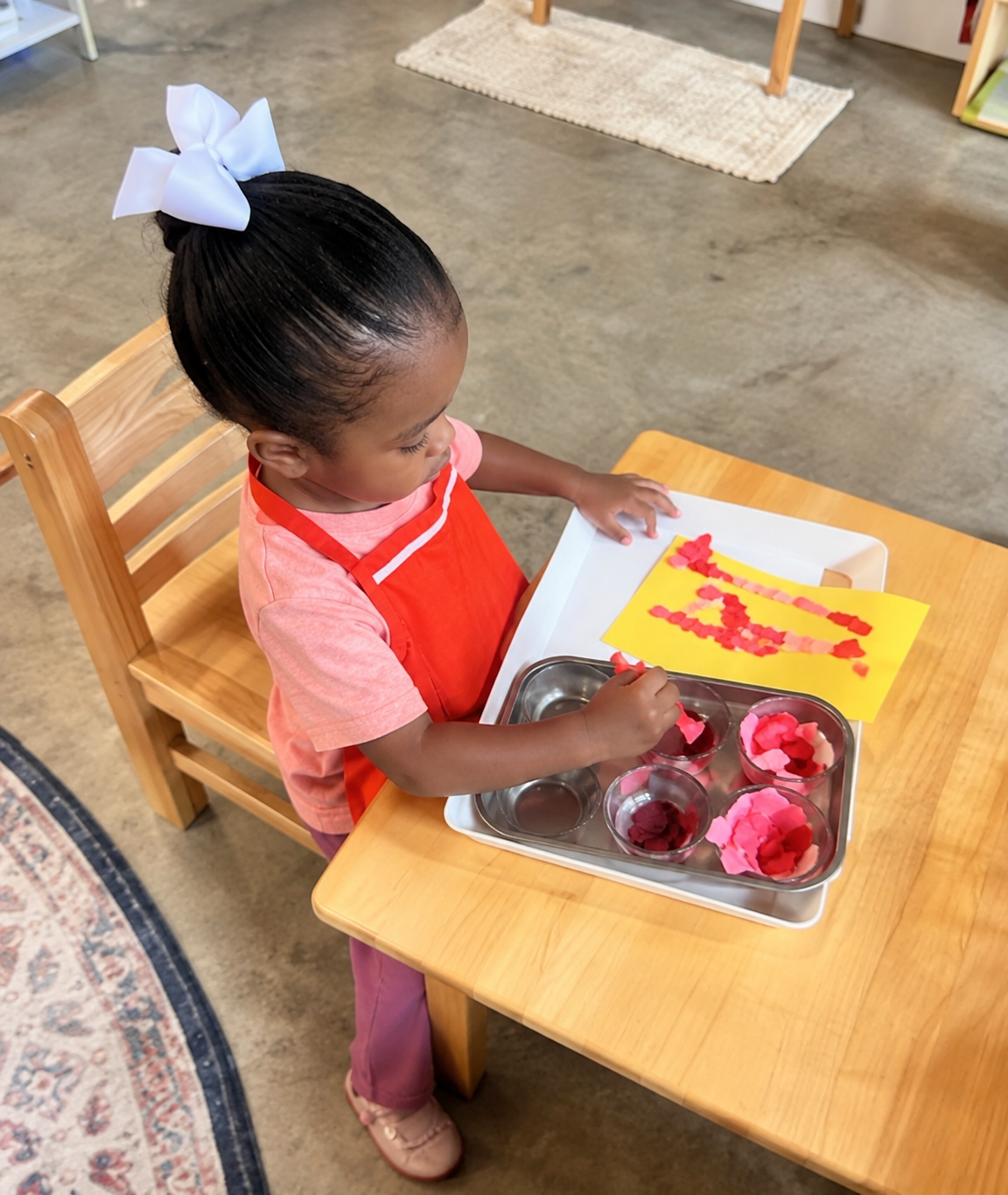 A toddler creating artwork with colorful materials at a child-sized table.