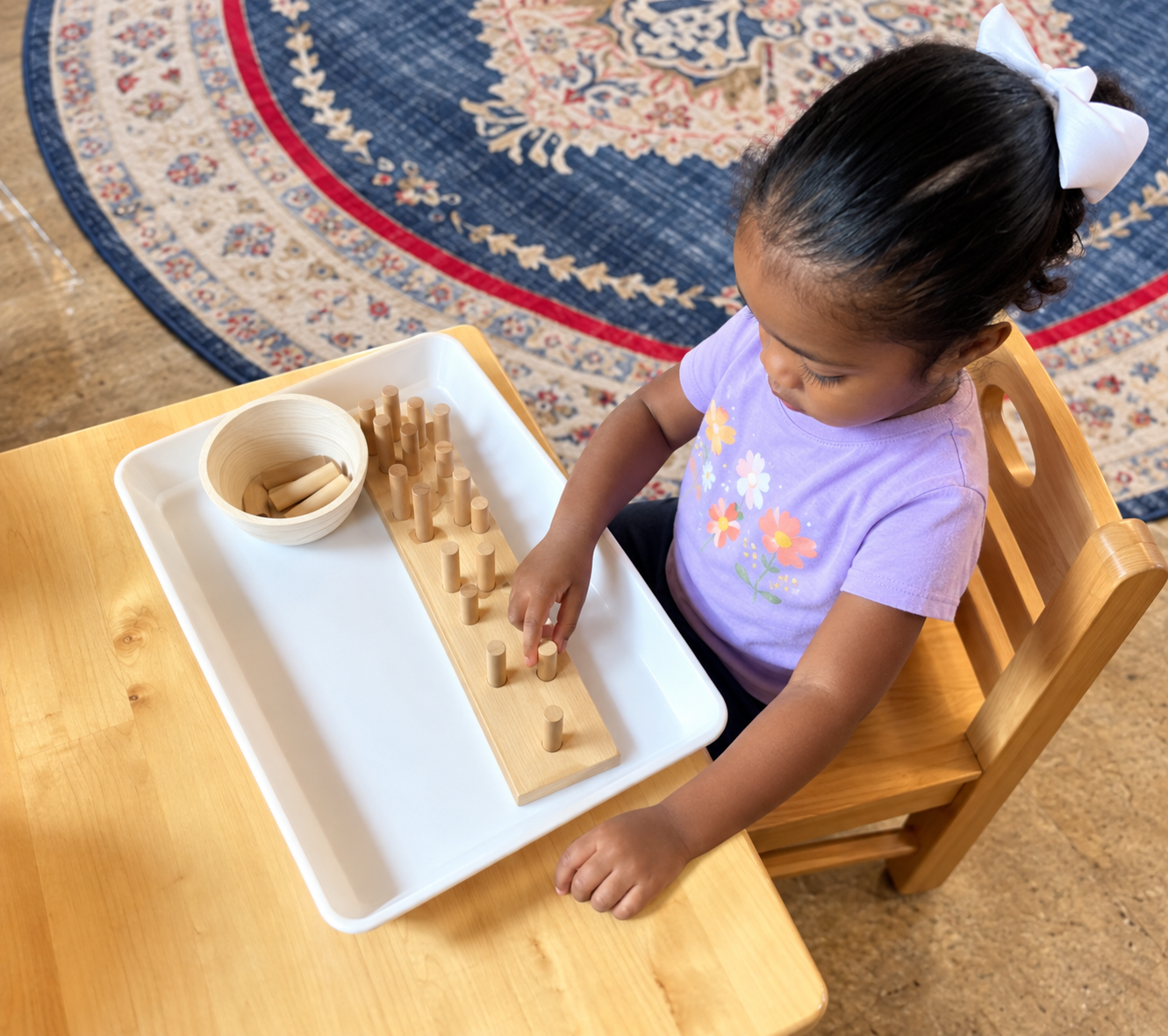 A toddler concentrating on a wooden Montessori cylinder activity.