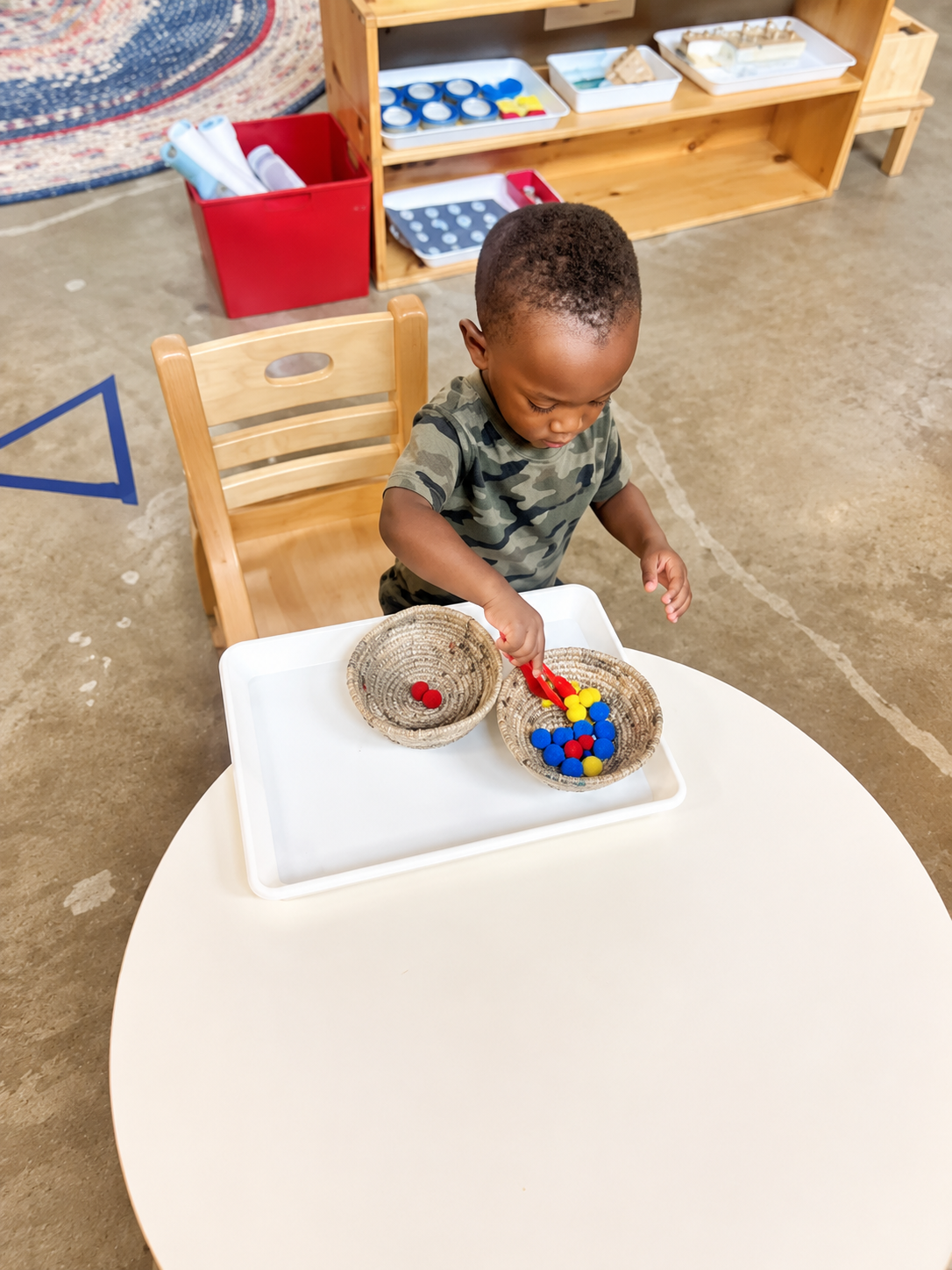 A toddler transferring colorful objects between baskets in the classroom.