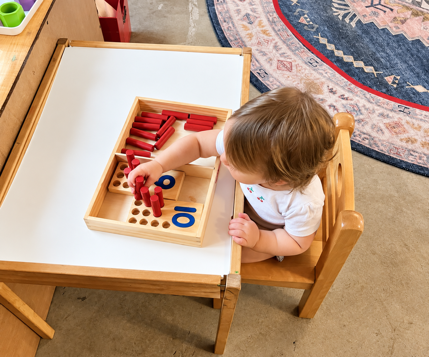 A toddler practicing a practical-life pouring activity with small metal pitchers.
